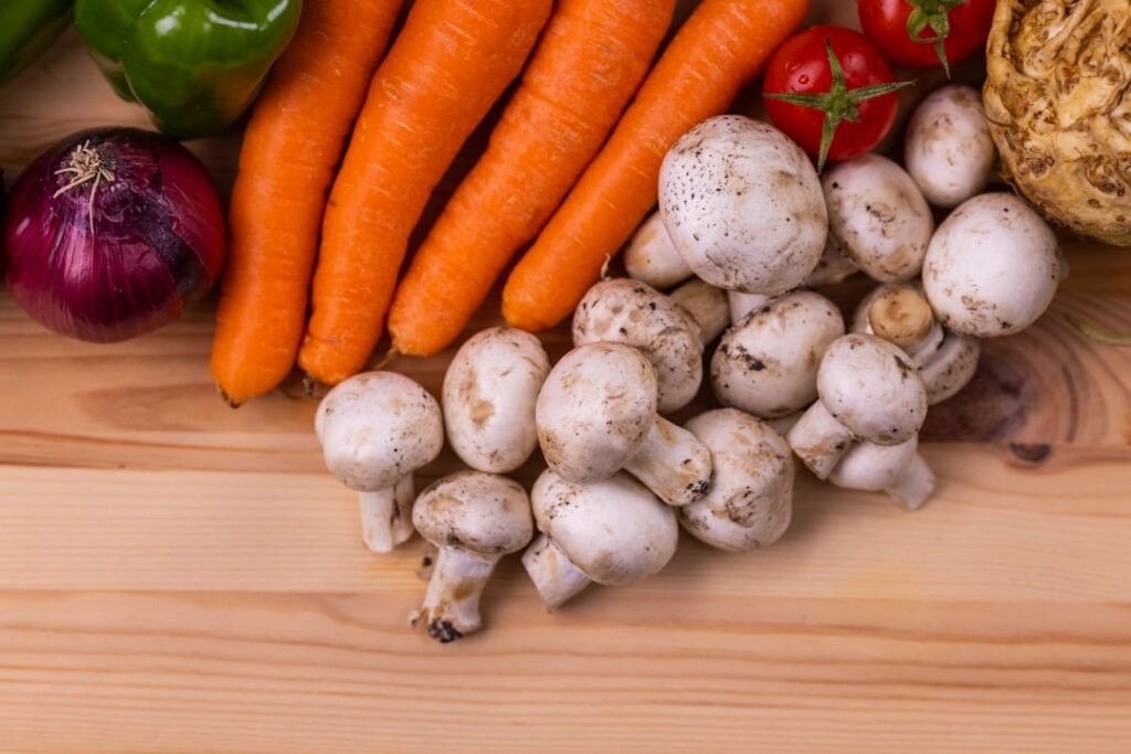 An overhead spread of fresh vegetables, whole grains, legumes, and nuts arranged on a wooden surface