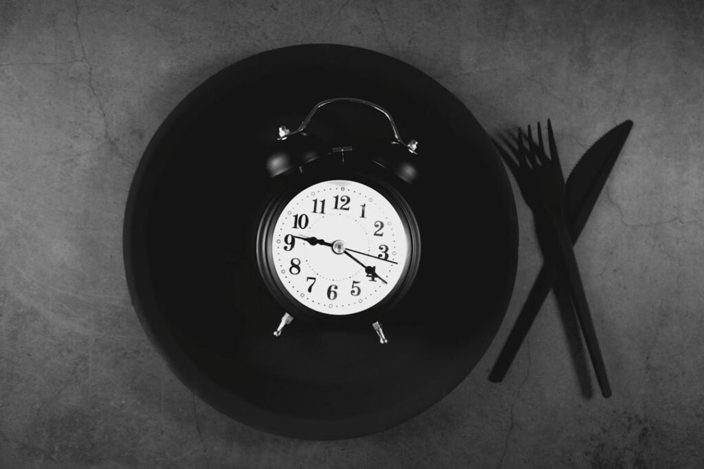 A simple plate and fork arranged beside a clock face on a plain background, suggesting time-based eating